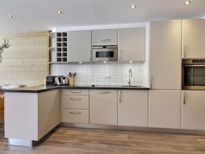 Cozinha moderna com armários brancos, micro-ondas, forno e painel de madeira.