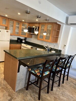 A modern kitchen with wooden cabinets, a granite countertop, and a central island with bar stools. - Entire Condominium - Newly upgraded Waikiki TOP Floor ILIKAI Hotel (Honolulu)