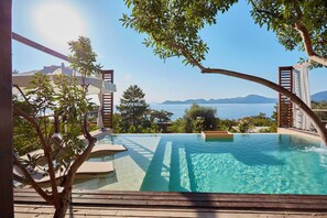 Una piscina infinita con vistas despejadas al mar y montañas al fondo.