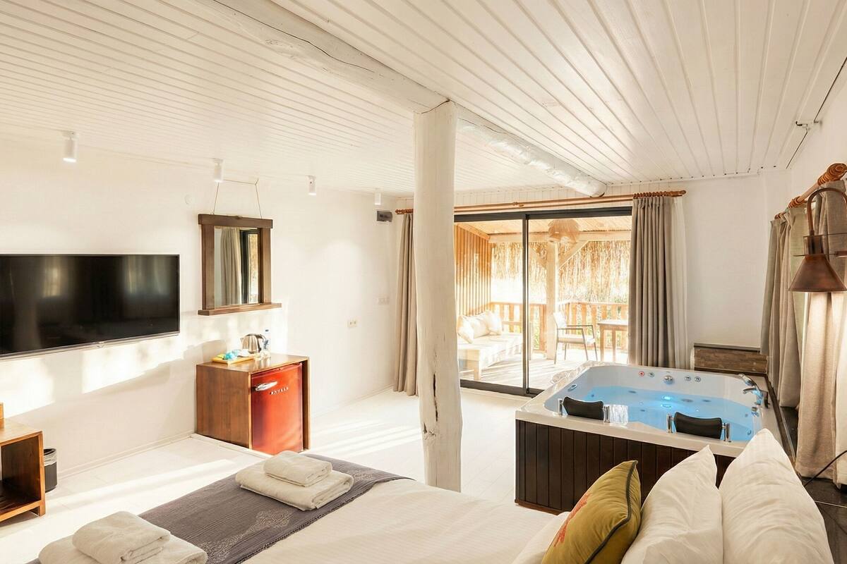 Une chambre d’hôtel dotée d’un grand lit, d’une télévision, d’un bureau, d’un minibar et d’un balcon avec un jacuzzi.
