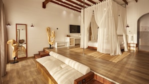 A spacious room with a large bed, a sitting area, and a television.