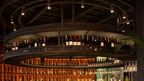 A bar area with a curved wooden counter, multiple seating options, and a wall of wine bottles.