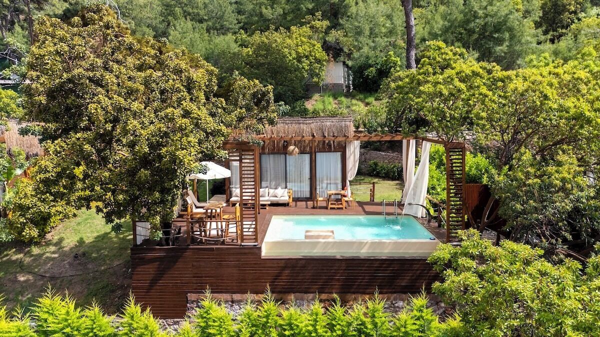 A hot tub surrounded by wooden deck, outdoor seating, and lush greenery.