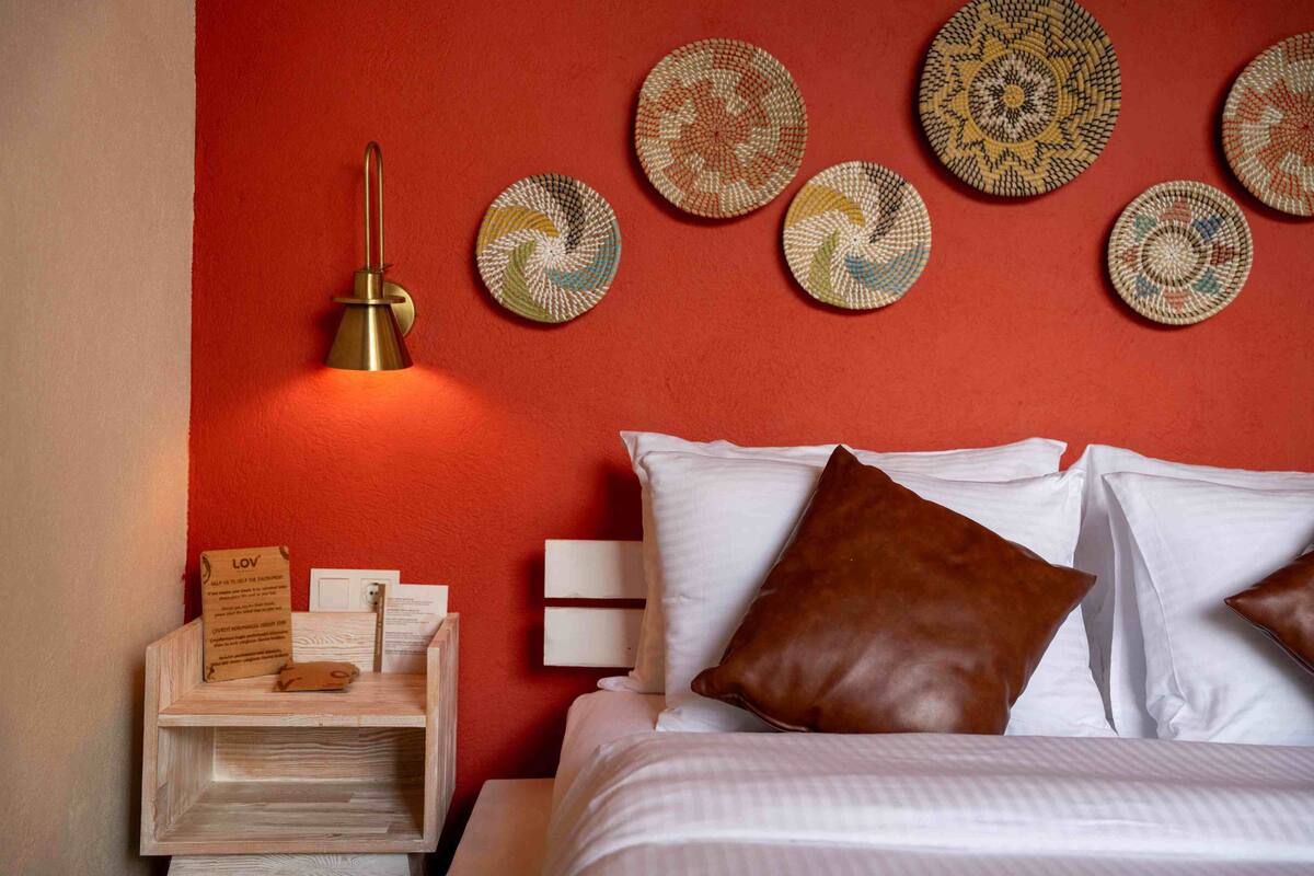 Une chambre d’hôtel bien rangée, avec un lit, des oreillers, une table de chevet avec une lampe et des assiettes décoratives accrochées au mur.