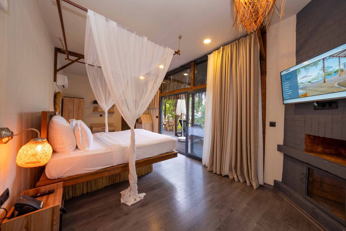 Une chambre à coucher avec un lit, une télévision, une cheminée et un balcon avec des rideaux.