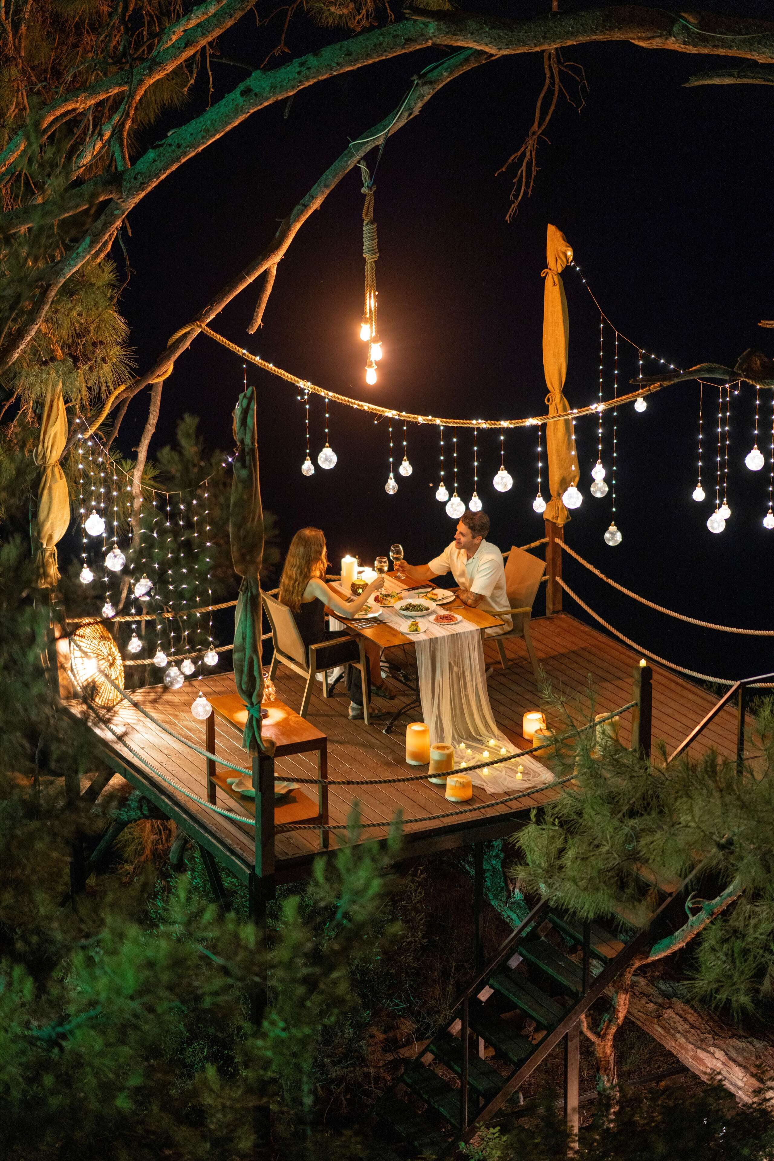An outdoor dining area with string lights, a table set for two, and a wooden deck.