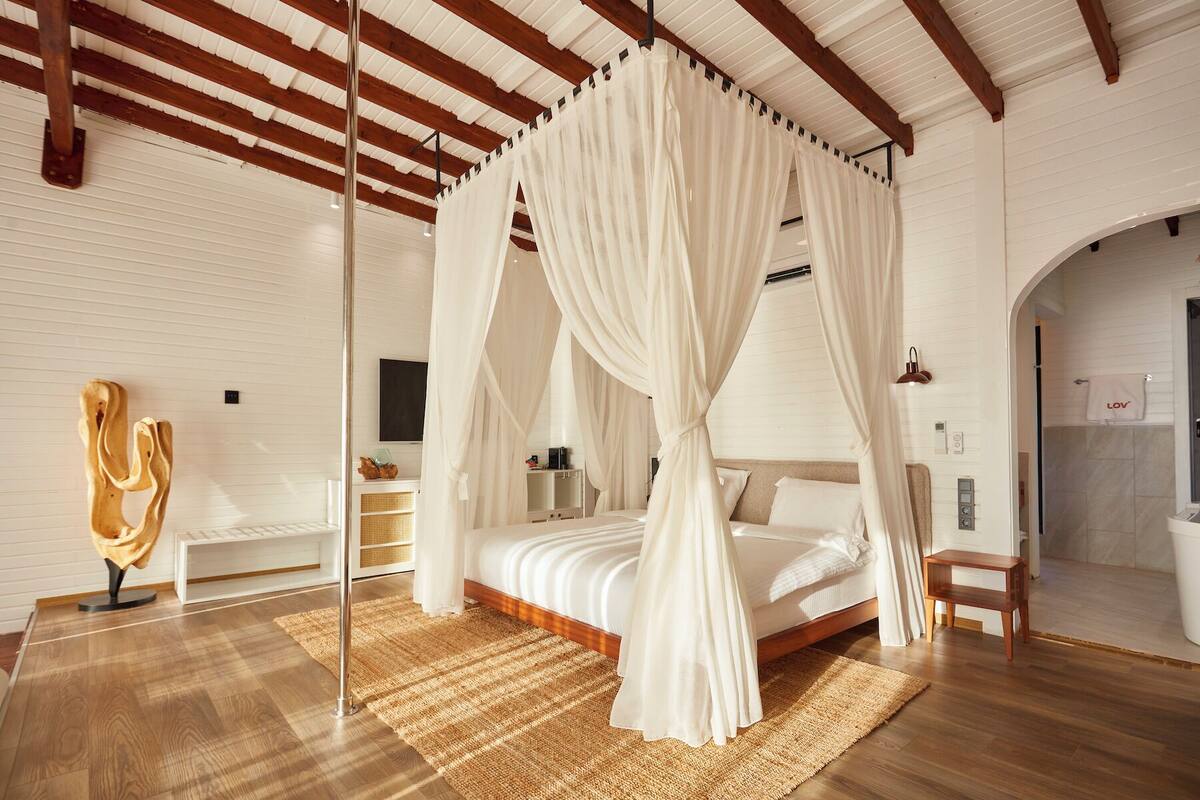 Une chambre à coucher avec un lit à baldaquin, un plancher en bois, un tapis tissé et un élément de décoration moderne.