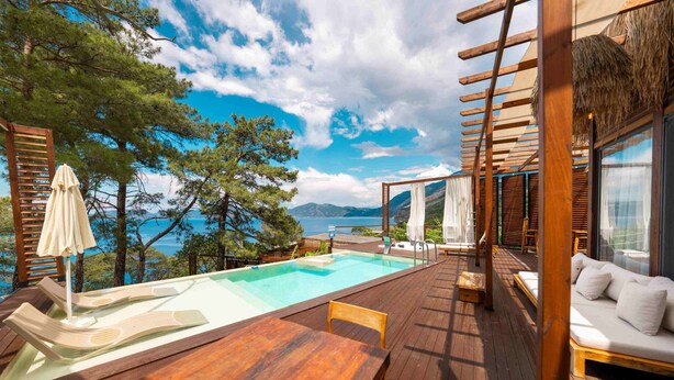 A wooden deck with a pool, lounge chairs, and a view of the sea.