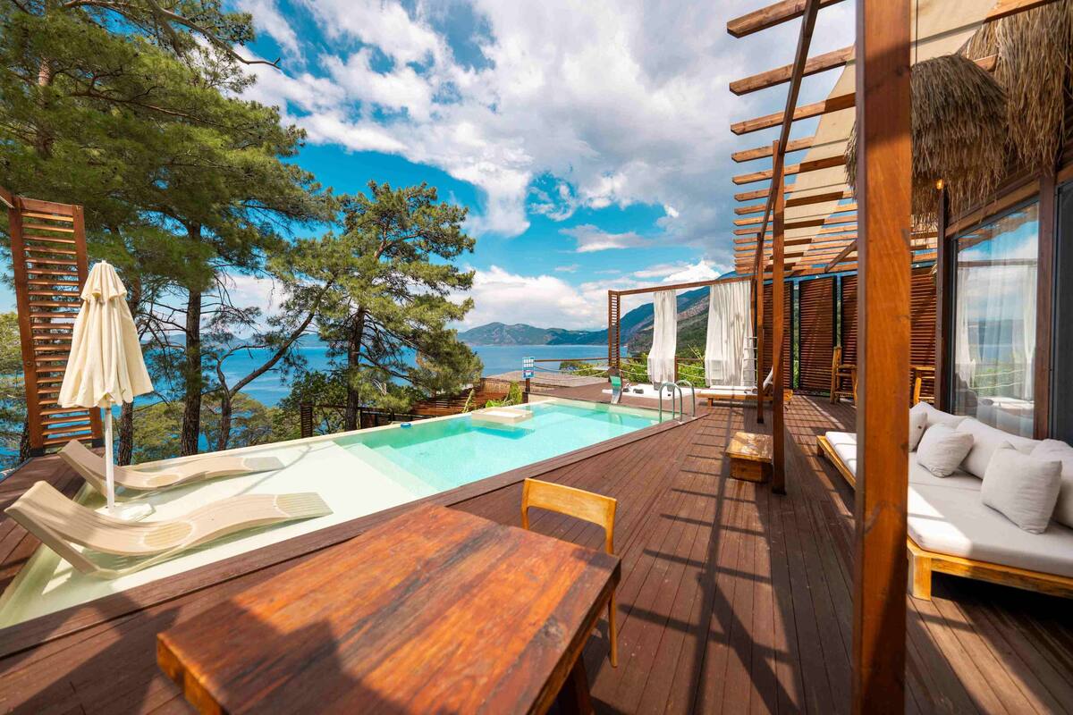 Une terrasse en bois avec une piscine, des chaises longues et une vue sur la mer.