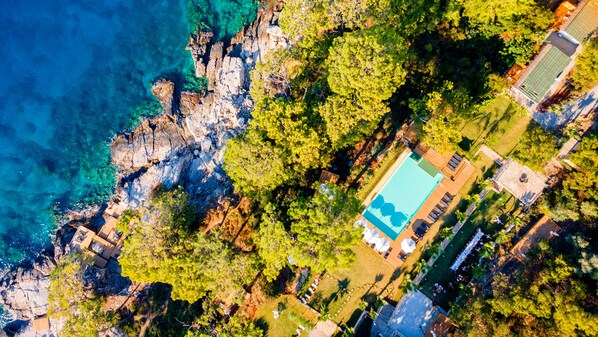 Relax in a tranquil coastal setting with a pool surrounded by lush greenery and scenic views.