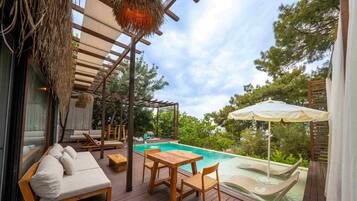 Terraza de madera con piscina, sillas de descanso y una mesa.