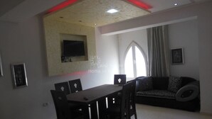 A living room with a dining table and chairs, a sofa, a TV mounted on the wall, and a window with curtains. - S+2 close to the sea chott meriem (Sousse)