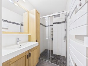 Ein modernes Badezimmer mit weiĂem Waschbecken, HolzschrĂ€nken, einer Duschkabine aus Glas und einem gefliesten Boden.