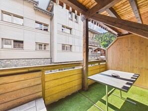 A balcony with a view of a building, a wooden table, and a stone wall.