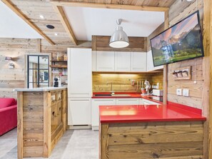 Une cuisine moderne avec des éléments en bois, un plan de travail rouge et un téléviseur fixé au mur.