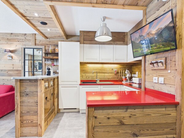 Eine moderne KĂŒche mit Holzelementen, einer roten Arbeitsplatte und einem wandmontierten Fernseher.