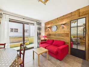 Ein gemĂŒtliches Wohnzimmer mit einem roten Sofa, einer Holzverkleidung, einer Uhr und Blick durch eine GlastĂŒr.