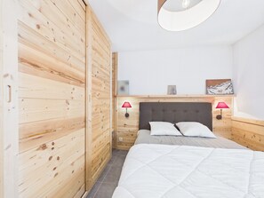 Ein Schlafzimmer mit einem Holzschrank, einem Bett mit weiĂer BettwĂ€sche, zwei Nachttischlampen und einem Wandbild.