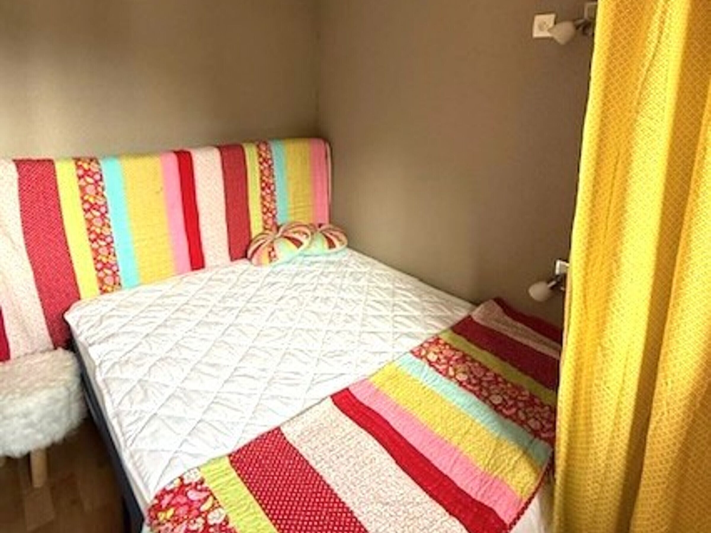 A bedroom with a bed, a colorful striped blanket, and a white quilt.