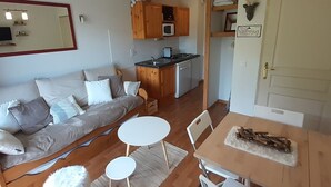 Un espacio habitable compacto con sofá, una mesa de comedor con sillas, una zona de cocina con armarios de madera y un refrigerador pequeño.