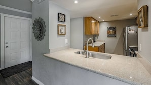 A modern kitchen with a granite countertop, stainless steel sink, and wooden cabinets.