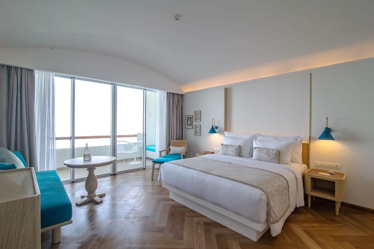 Une chambre d’hôtel avec un grand lit, une petite table ronde, une chaise et un balcon avec vue.