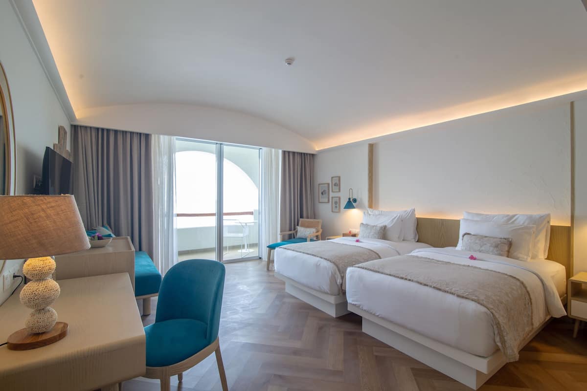 Une chambre d’hôtel avec deux lits, un bureau avec une lampe, une chaise et une vue sur l’extérieur.