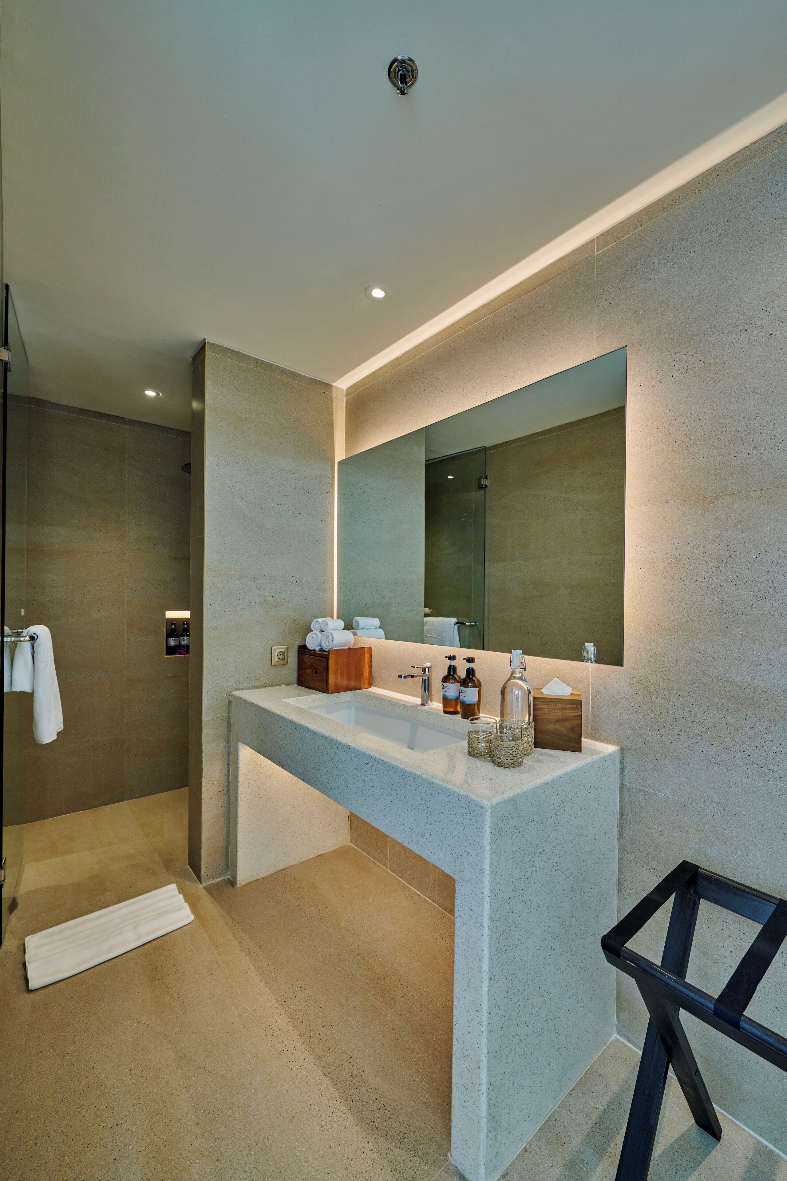 A modern bathroom with a large mirror, a countertop with toiletries, and a shower area.