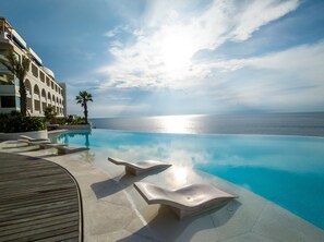 A pool with a view of the ocean, a building with balconies, and palm trees. - Royal Avila Boutique Resort (Senggigi)