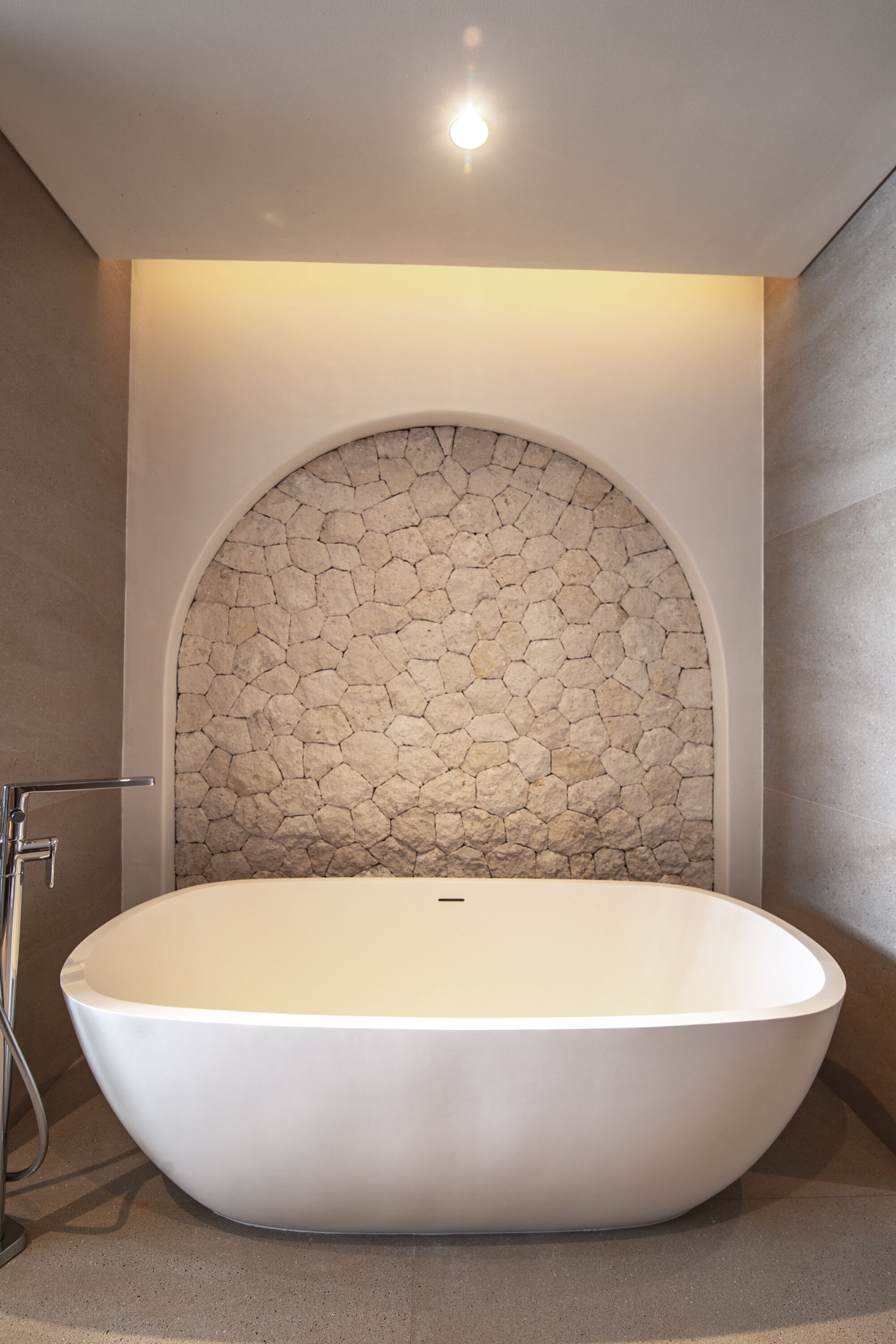 Un baño moderno con una bañera independiente, un muro de mosaicos de piedra e iluminación empotrada en el techo.