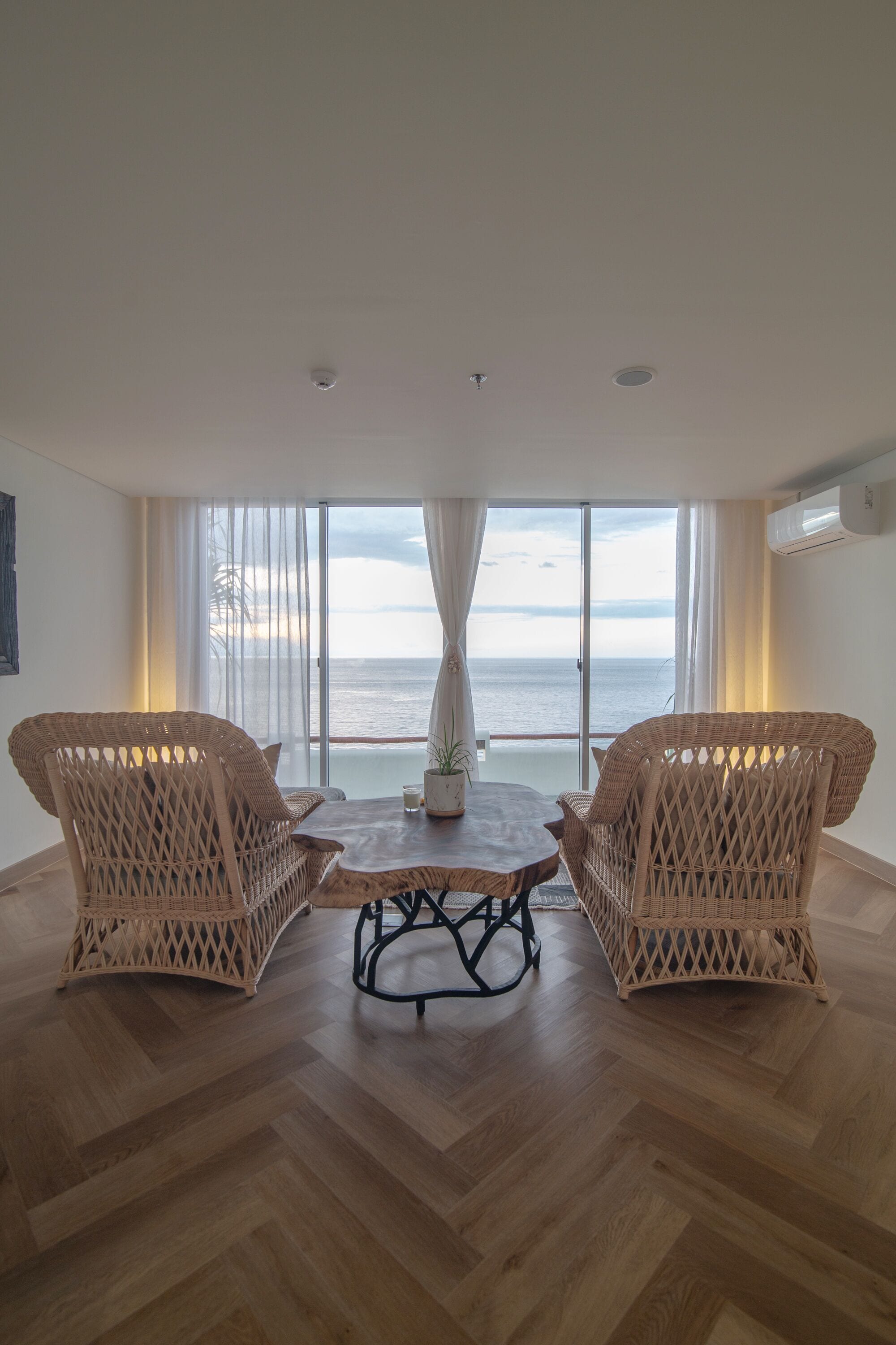 Una habitación con dos sillas de mimbre, una mesa de madera y vista al mar a través de amplios ventanales.