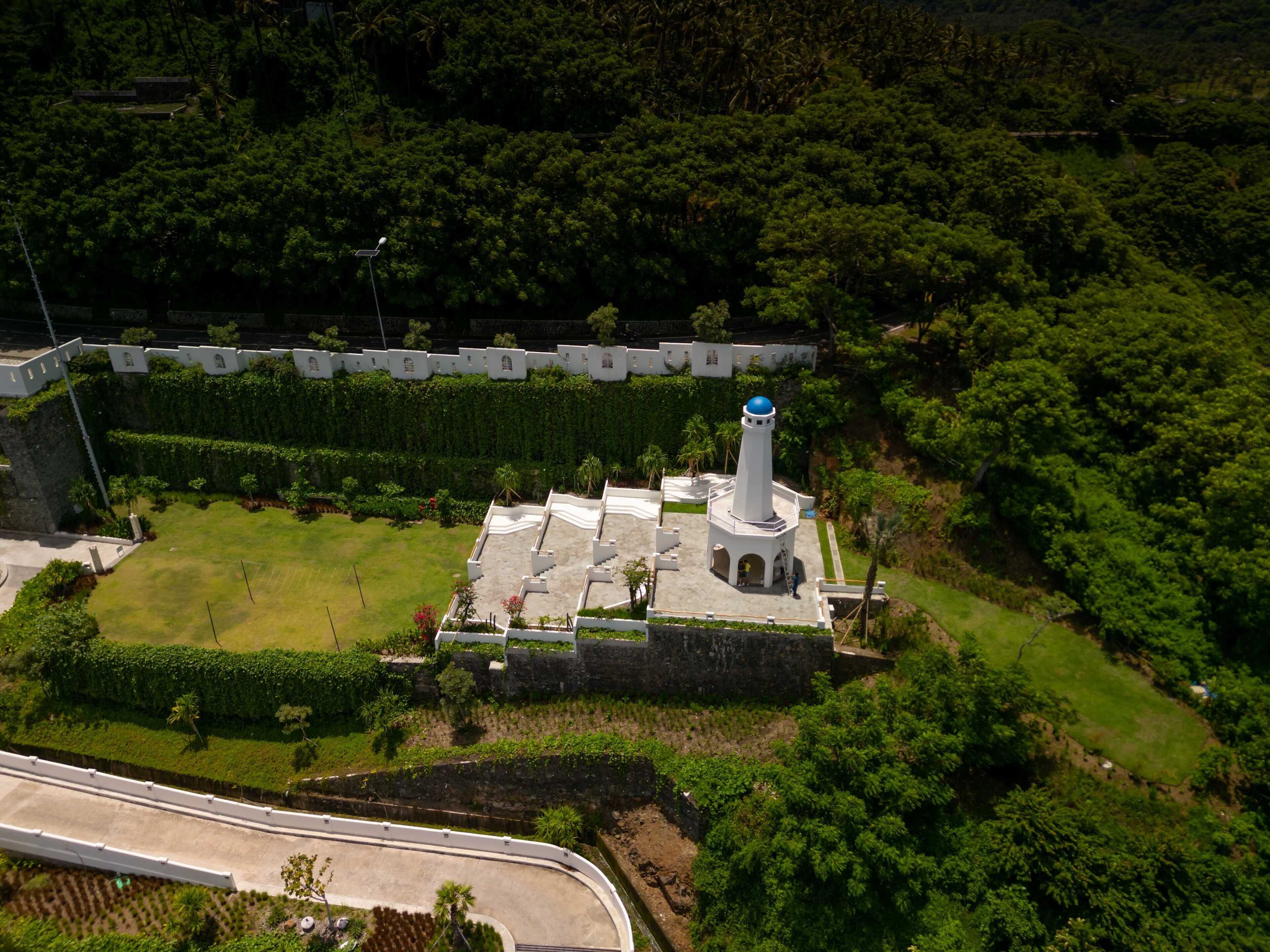 An aerial view of a historic fort with a prominent tower, surrounded by lush greenery and a well-maintained garden.
