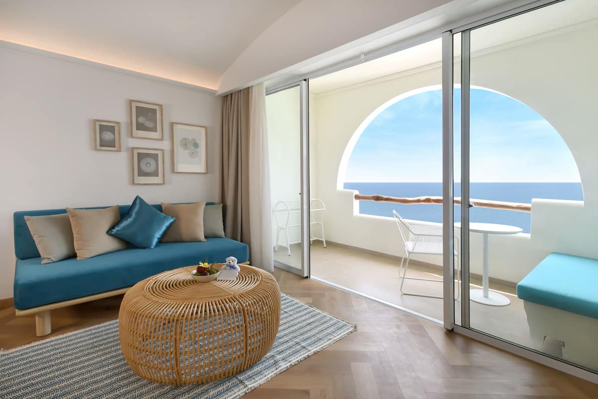 Un salon moderne avec un canapé, une table basse ronde et un balcon offrant une vue sur la mer.