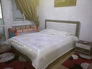 Une chambre à coucher comprenant un lit, une table de chevet, une commode, une fenêtre avec des rideaux, une bibliothèque et un tableau accroché au mur.