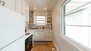 A compact kitchen with white cabinets, a stove, and a window providing natural light. - Cute Home in the Heart of Missoula! (Missoula)