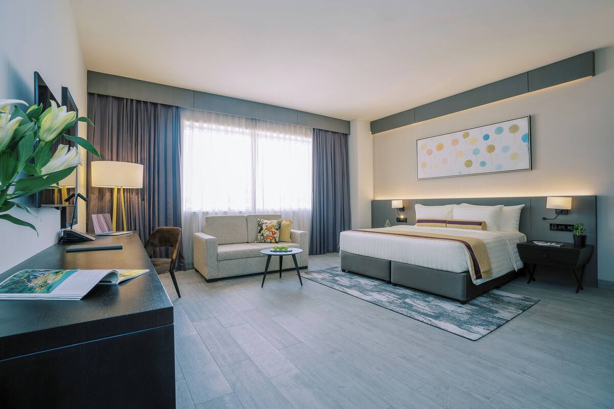 A modern hotel room with a bed, a sofa, a desk, and a large window with curtains.