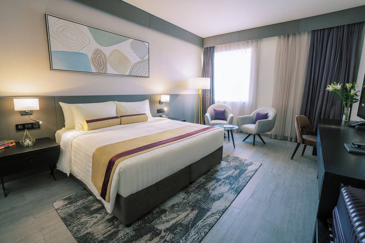 A hotel room with a large bed, two bedside tables, a desk, a chair, and a TV.
