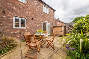 A brick house with a patio area featuring wooden furniture and plants.