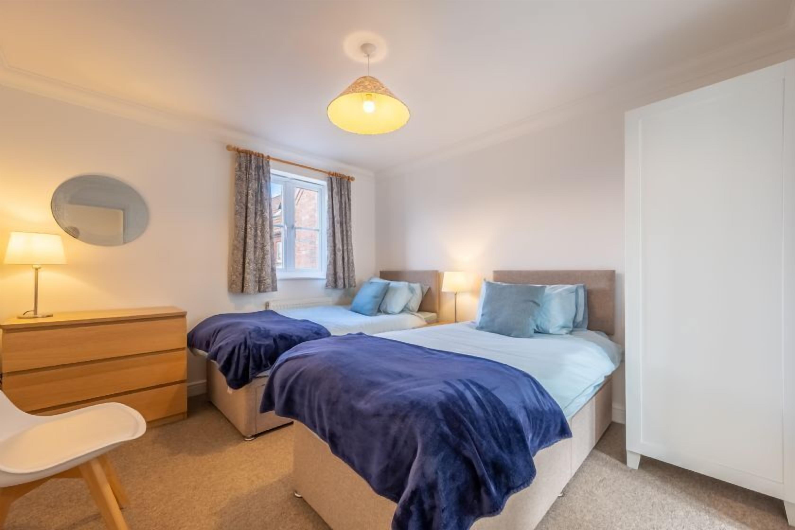 A bedroom with two beds, a desk, a chair, a lamp, and a window with curtains.