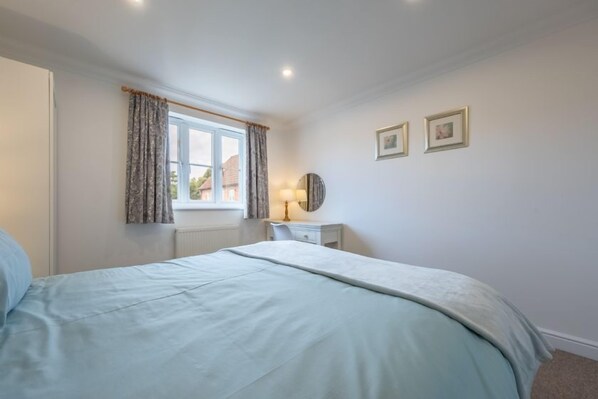 Une chambre à coucher avec un lit, une fenêtre avec des rideaux, une table de chevet avec une lampe, et deux tableaux encadrés accrochés au mur.