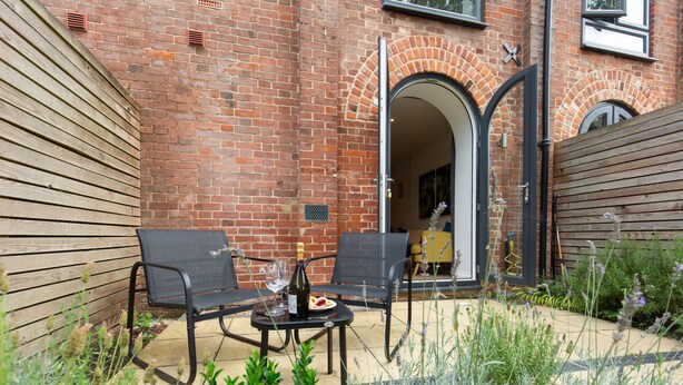 Eine Terrasse im Freien mit zwei schwarzen Metallstühlen, einem kleinen Tisch, einer Weinflasche und einem Glas.