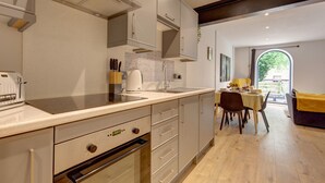 Eine moderne Küche mit Backofen, Kaffeemaschine und Spüle. Ein Essbereich mit Tisch und Stühlen ist ebenfalls vorhanden.