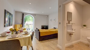 Ein modernes Hotelzimmer mit Essbereich, einem Bett mit gelber Decke, einem Fernseher und einem Badezimmer mit Waschbecken und Spiegel.