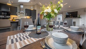 A modern kitchen with dark cabinets, a microwave, and a dining area set with white and patterned tableware, a wine bottle, and a floral centerpiece. - Field Lodge, Burnham Market, Norfolk (Burnham Market)