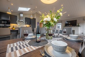 Eine moderne Küche mit dunklen Schränken, einer Mikrowelle und einem Essbereich, gedeckt mit weißem und gemustertem Geschirr, einer Weinflasche und einem floralen Mittelstück.