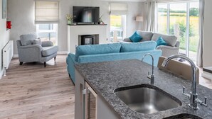 A modern kitchen with a granite countertop, a built-in sink, and a flat-screen TV above the fireplace. - Field Lodge, Burnham Market, Norfolk (Burnham Market)