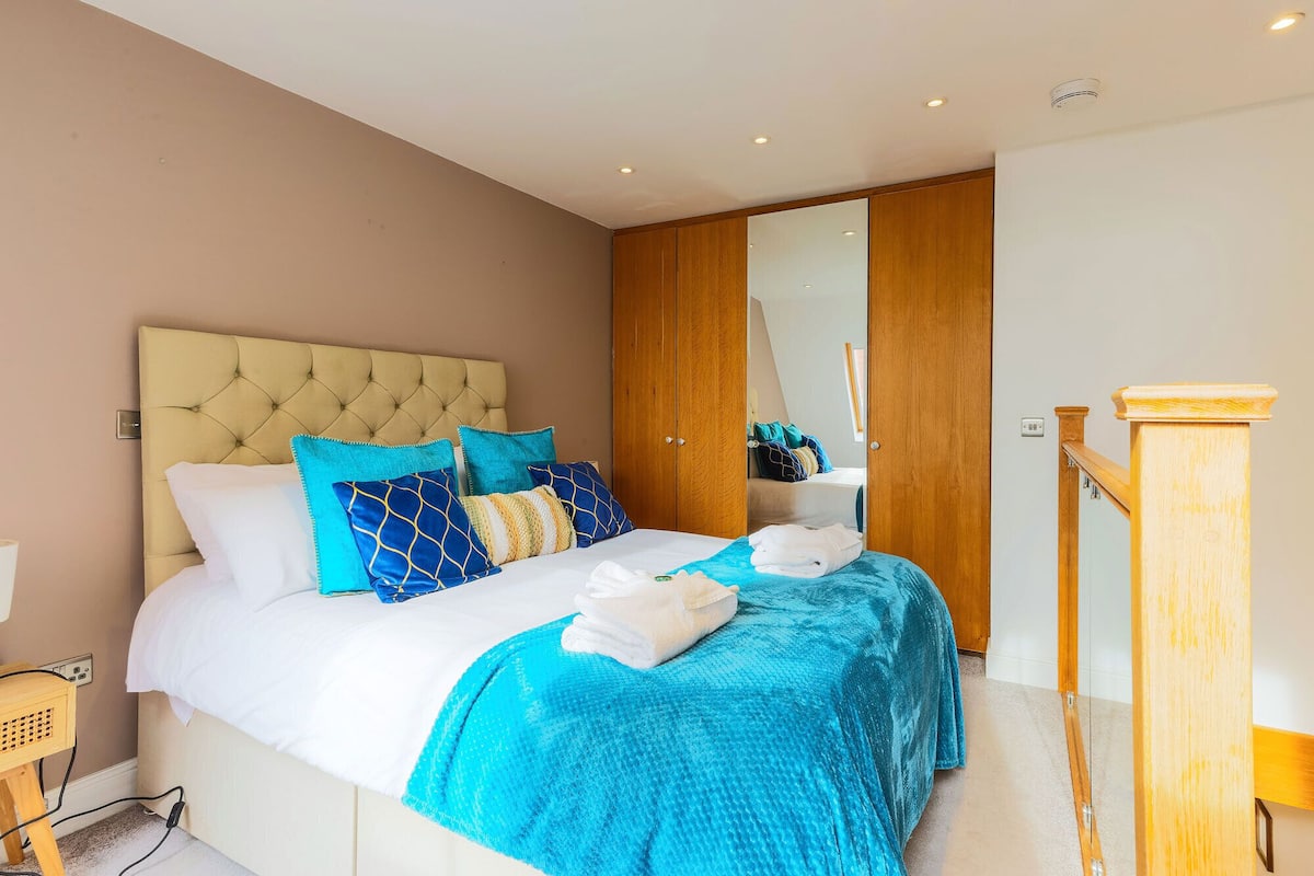 A bedroom with a tufted headboard, a bed with blue and white bedding, a wooden wardrobe, and a wooden bedside table.