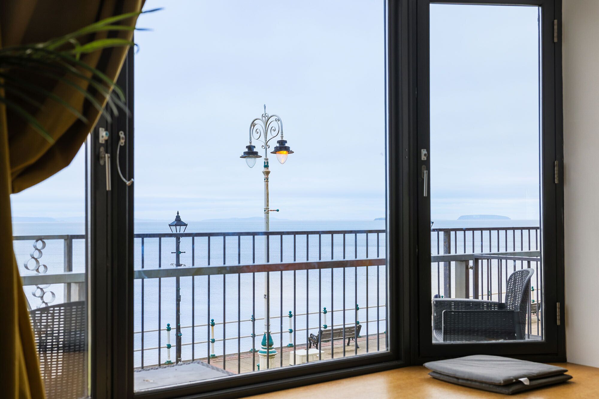 Un balcón con vista al mar, una banca y una mesa.