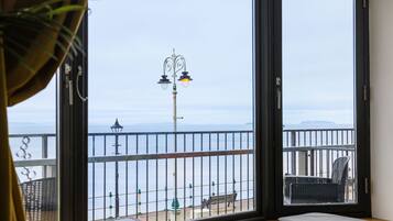 Un balcón con vista al mar, una banca y una mesa.