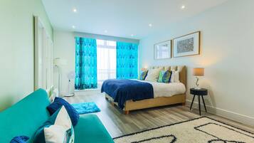 Un dormitorio moderno con cama, sofá, ventilador y ventana con cortinas.